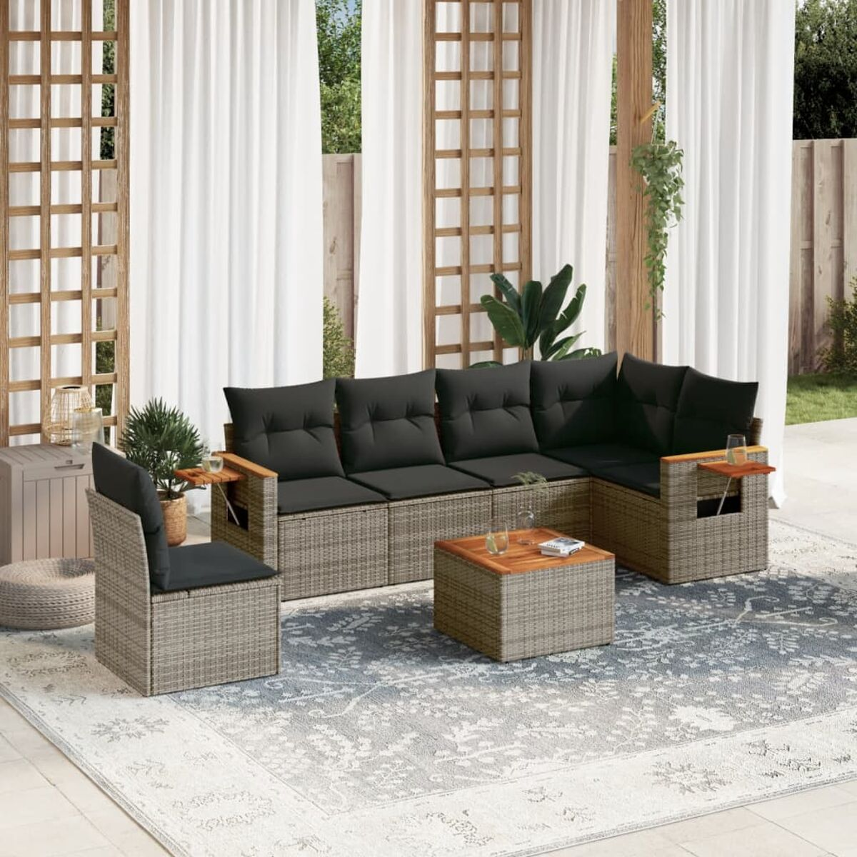 Gartenmöbel-Set aus Korbgeflecht mit grauen Kissen, Teppich und weißen Vorhängen im Hintergrund.
