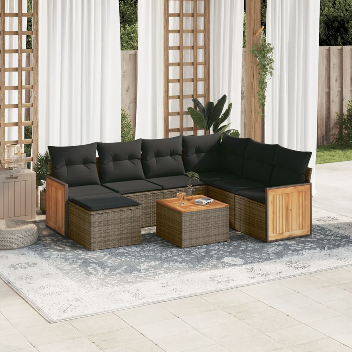 Rattan-Sofa-Set für den Außenbereich mit schwarzen Kissen, Holzakzenten und Couchtisch. Teppich, Vorhänge und Holzstruktur im Hintergrund.