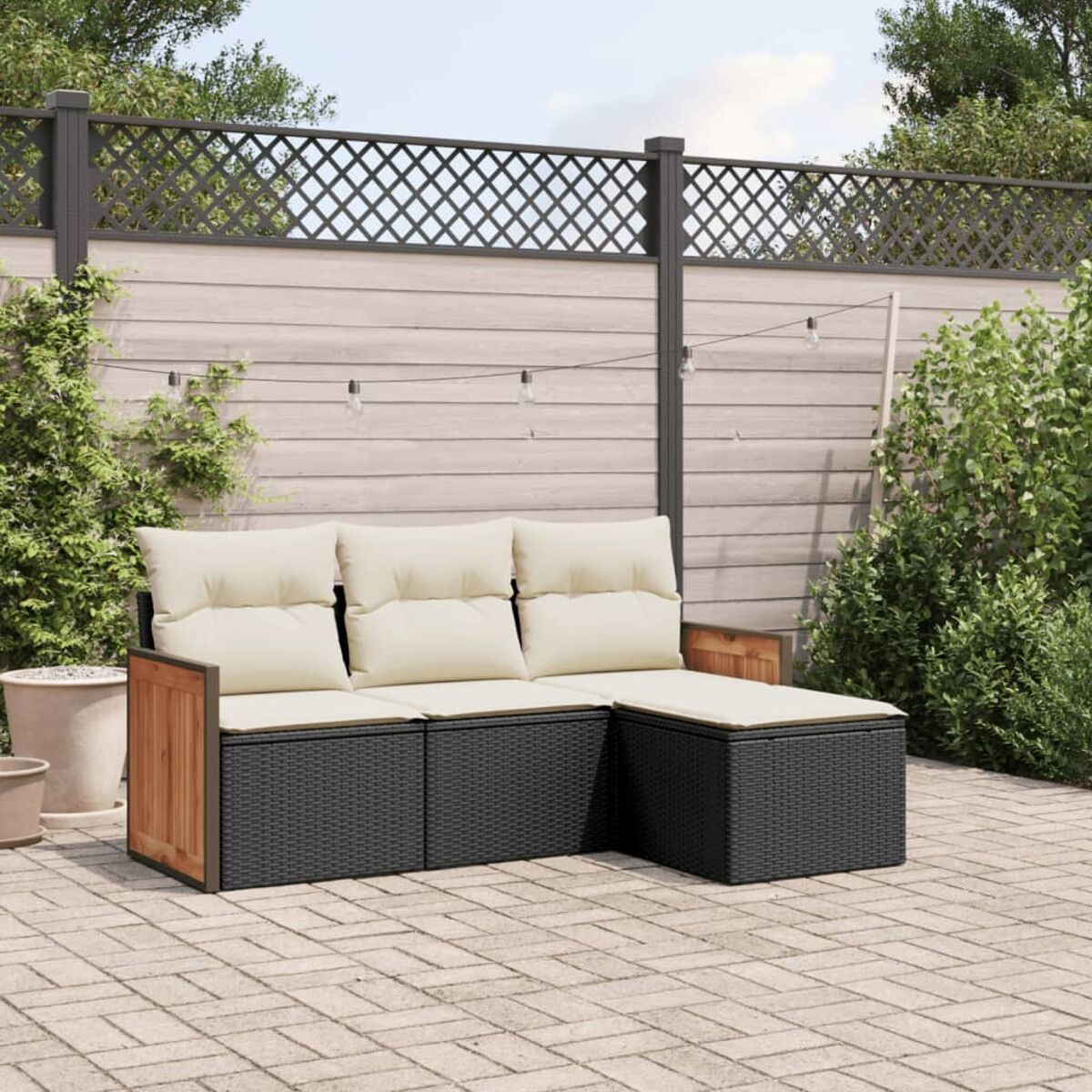 Schwarzes Korbsessel-Sofa mit cremefarbenen Kissen auf einer Terrasse. Der Garten hat einen Zaun und Pflanzen.