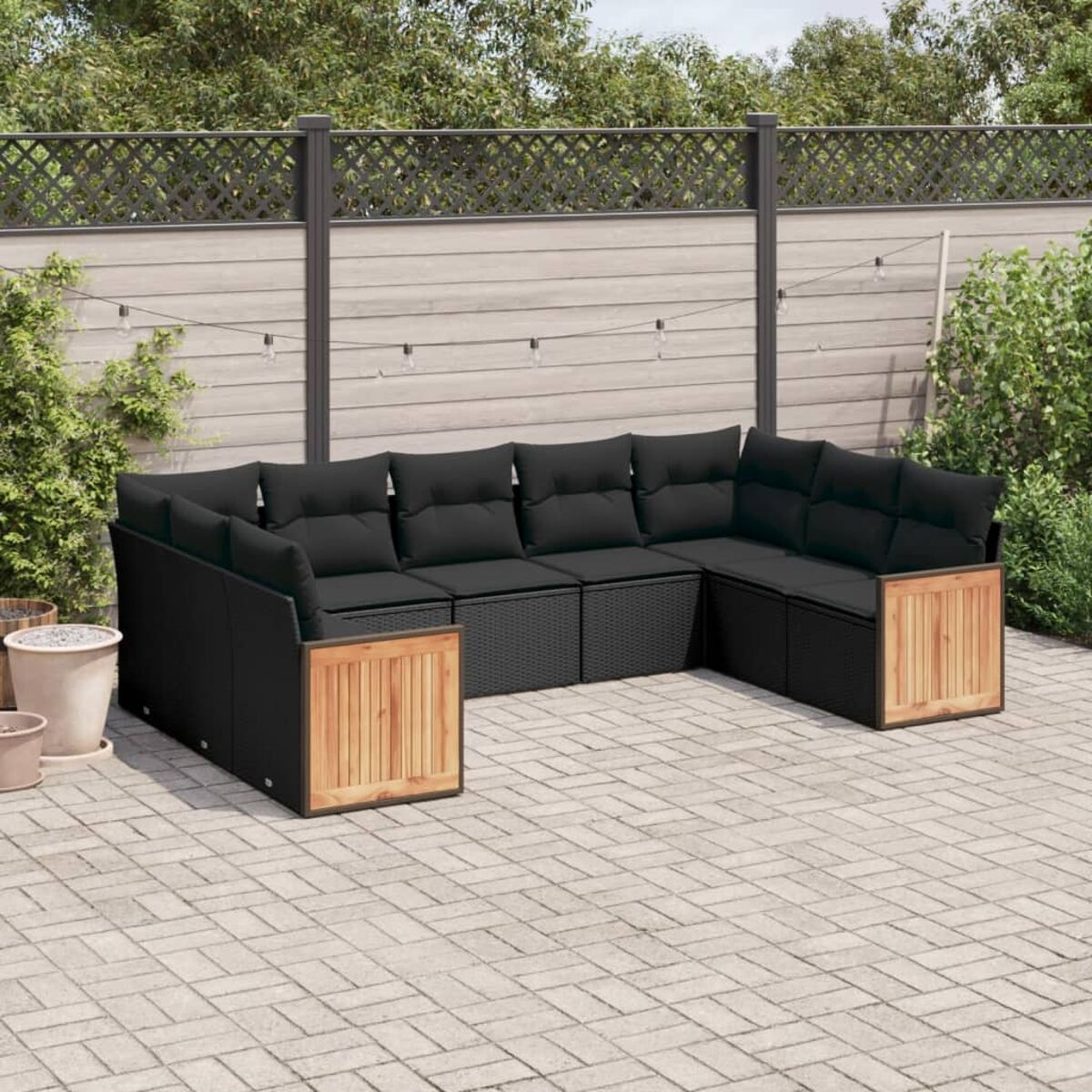 Gartensitzgruppe: schwarzes Rattan-Ecksofa mit schwarzen Kissen und Holzakzenten. Auf Ziegelterrasse mit Zaun.