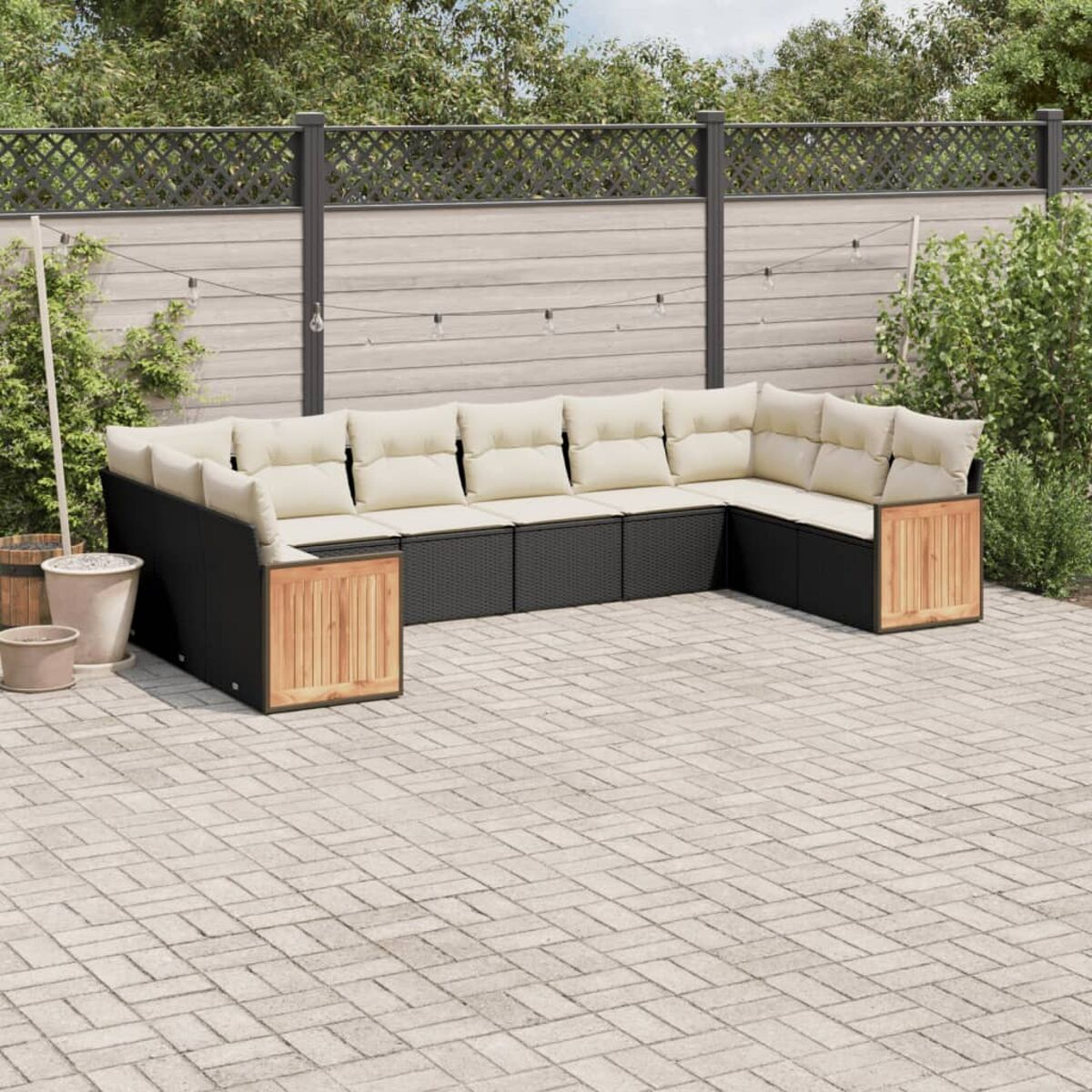 Schwarzes Outdoor-Sofa mit beigen Kissen. Holzakzente und Backstein-Patio mit Zaun im Hintergrund.