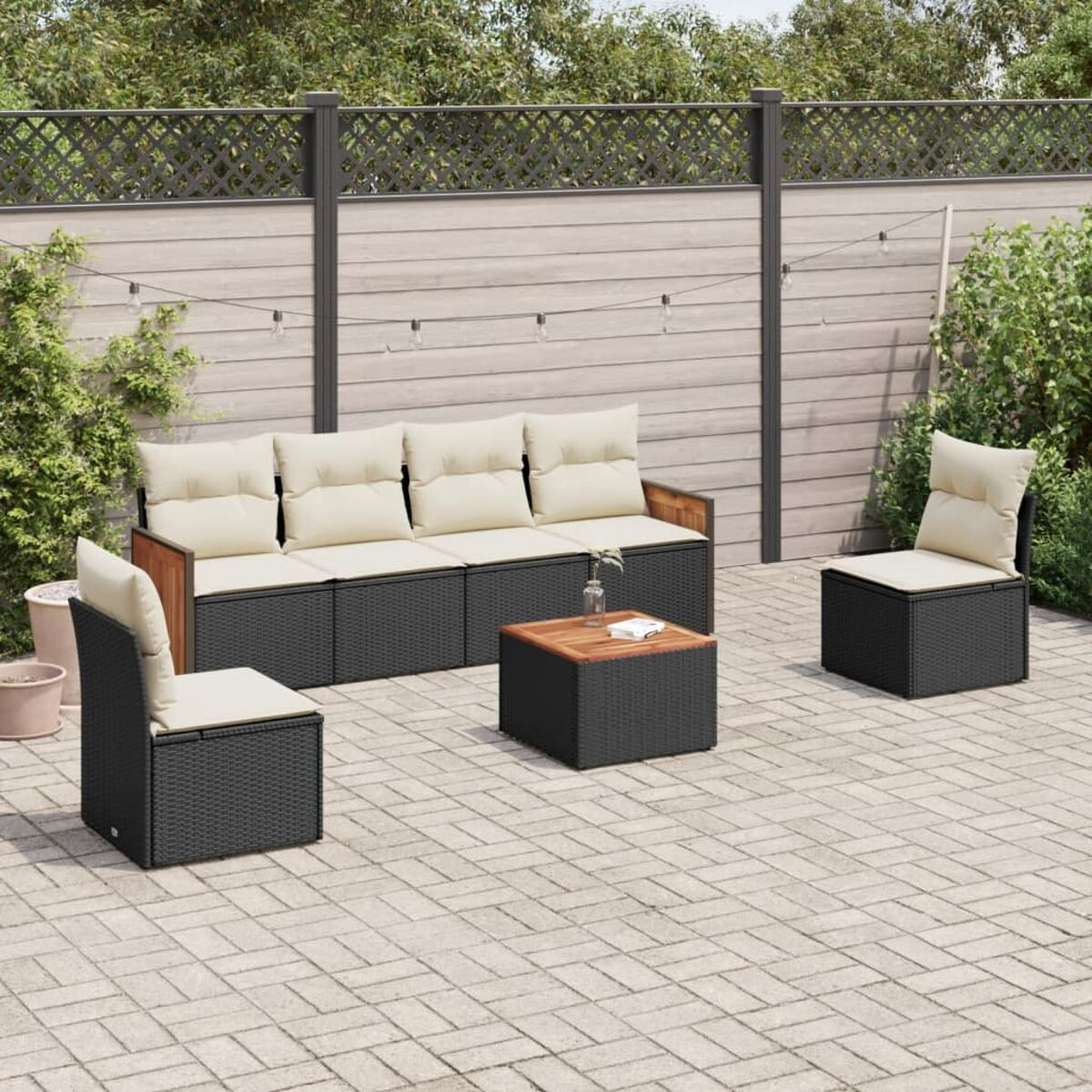 Terrassenmöbel mit schwarzen Stühlen, Sofa und Holztisch auf Pflastersteinen.