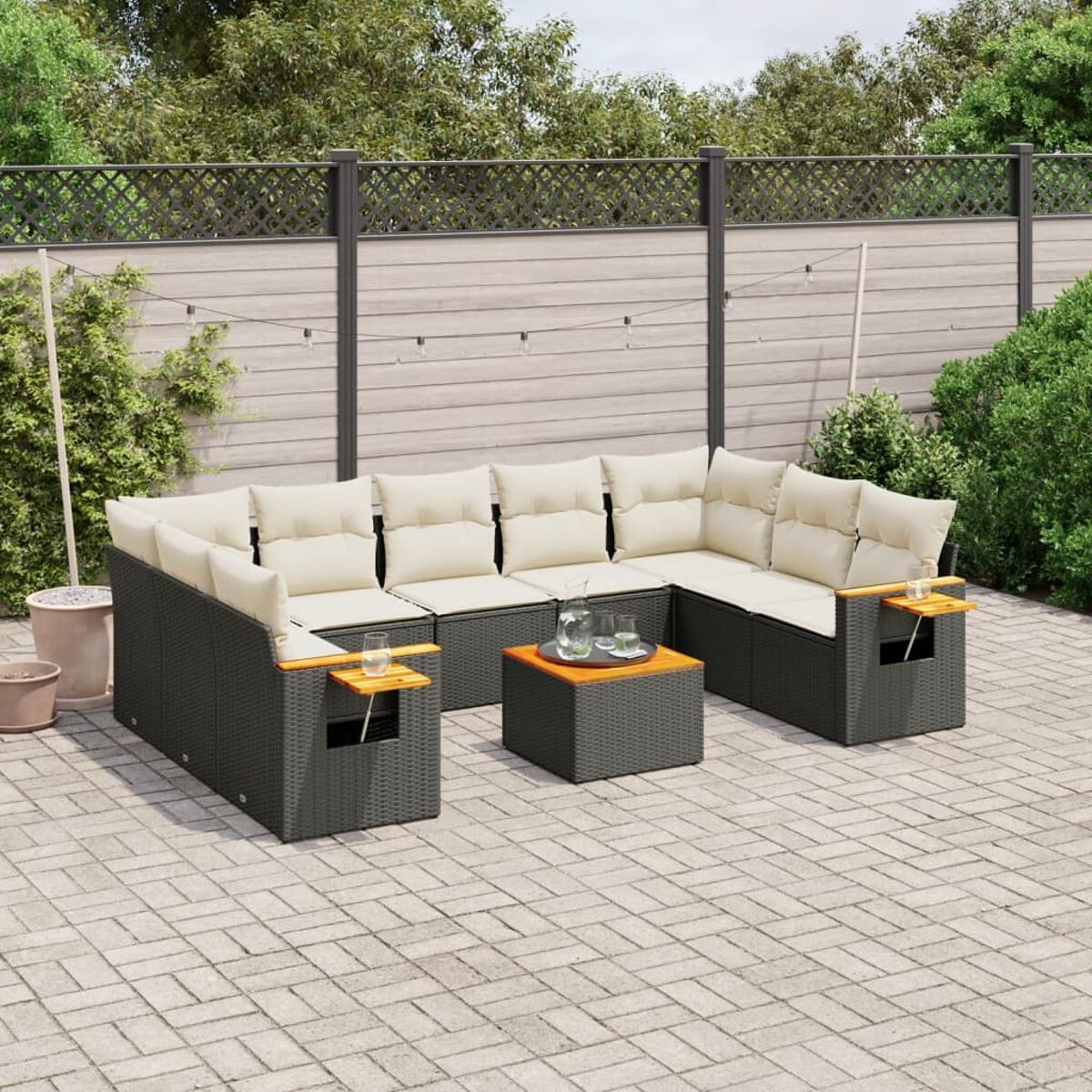 Schwarzes Ecksofa aus Rattan mit cremefarbenen Kissen und Beistelltischen auf einer Backstein-Terrasse.