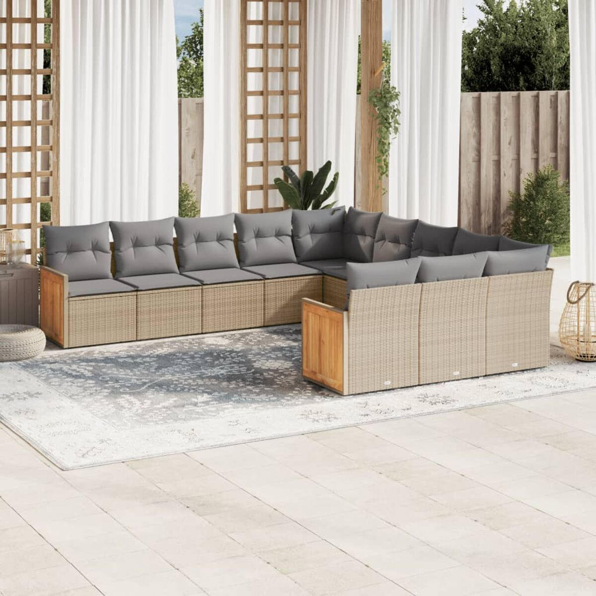 Beiges Outdoor-Möbel-Set aus Korbgeflecht auf einem gemusterten Teppich, mit weißen Vorhängen und Pflanzen.