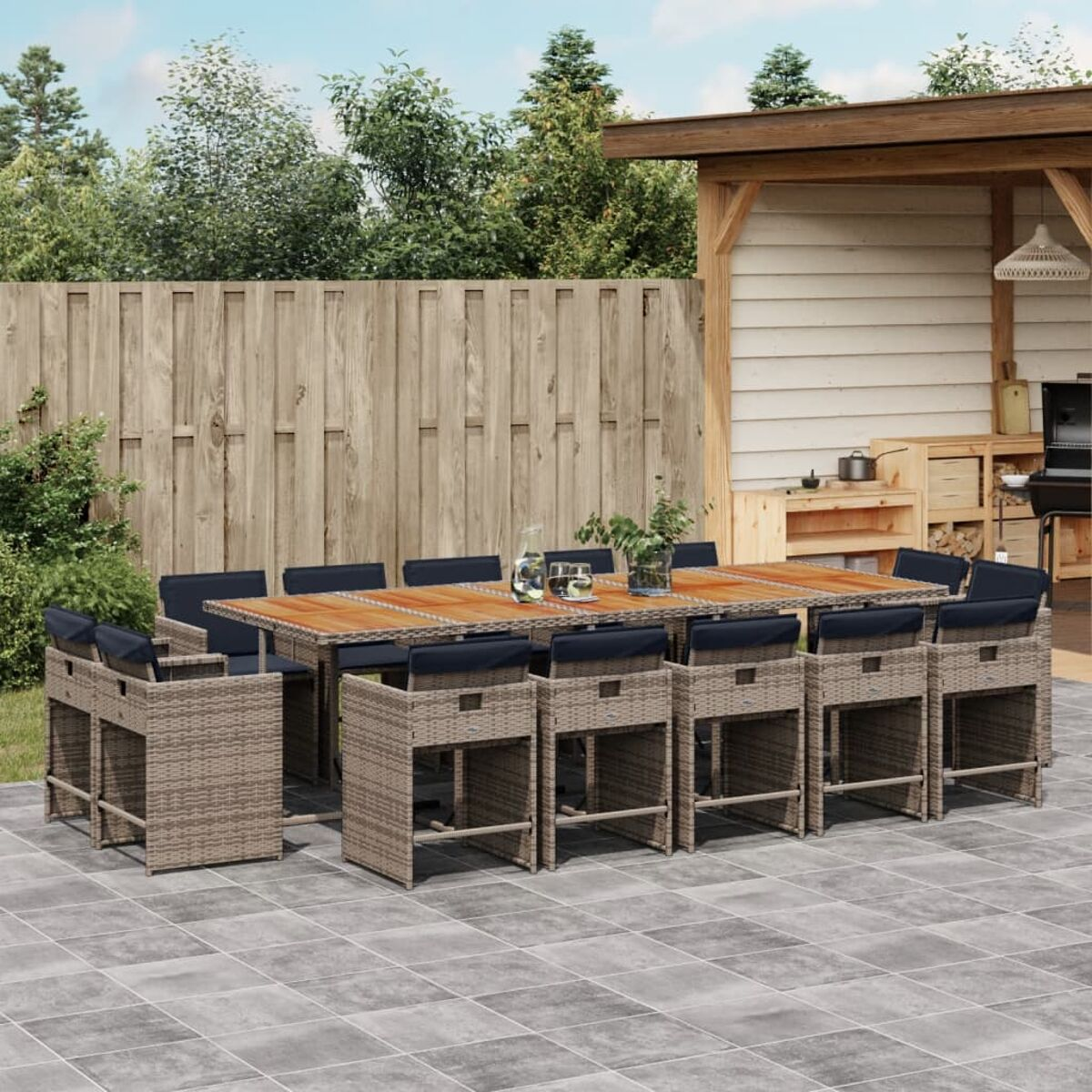 Essgruppe für den Außenbereich: Tisch mit 10 Barhockern. Tisch aus Holz. Hocker aus Korbgeflecht mit blauen Kissen.