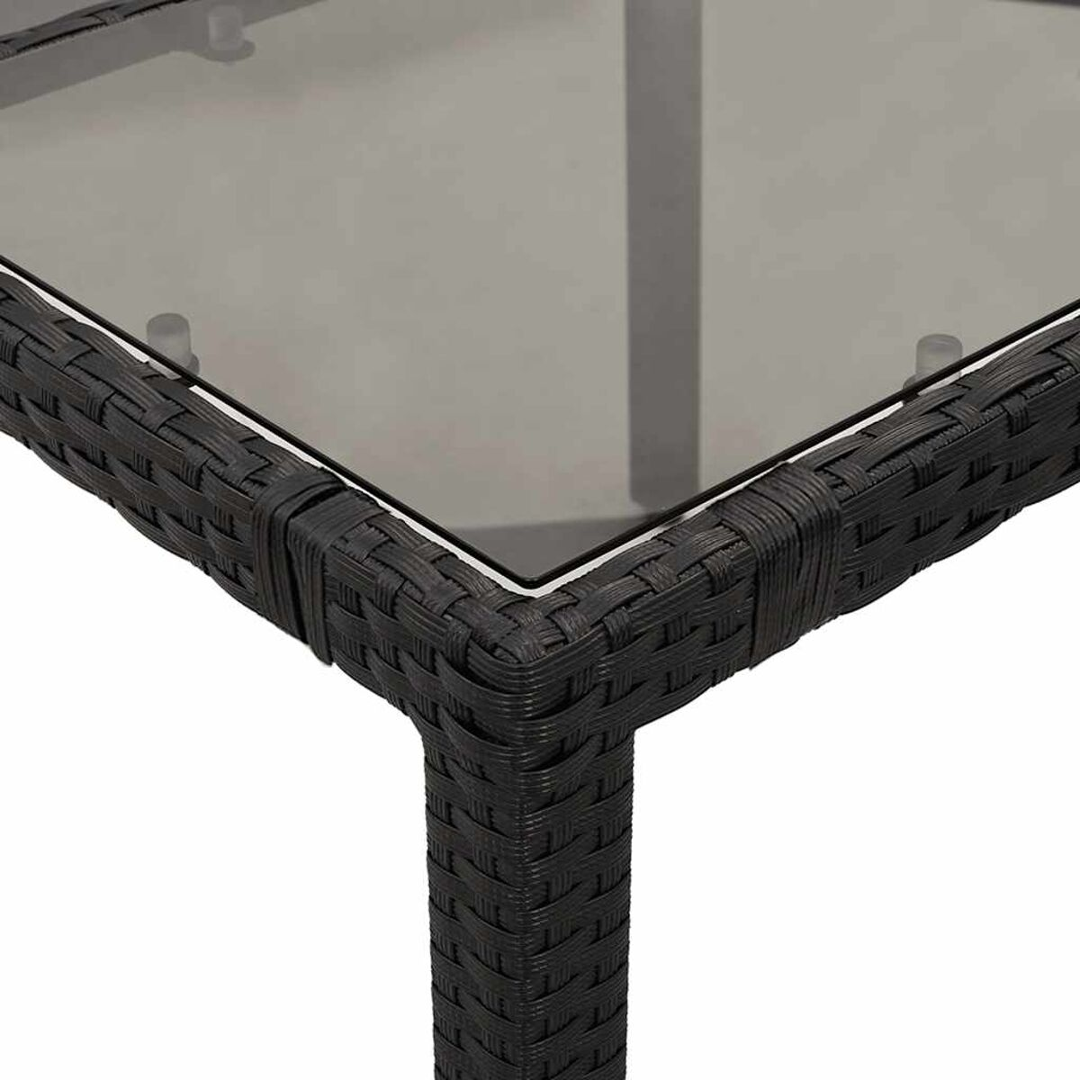 Primo piano di un angolo di tavolo quadrato. Struttura in rattan nero intrecciato con piano in vetro, bordi bianchi.