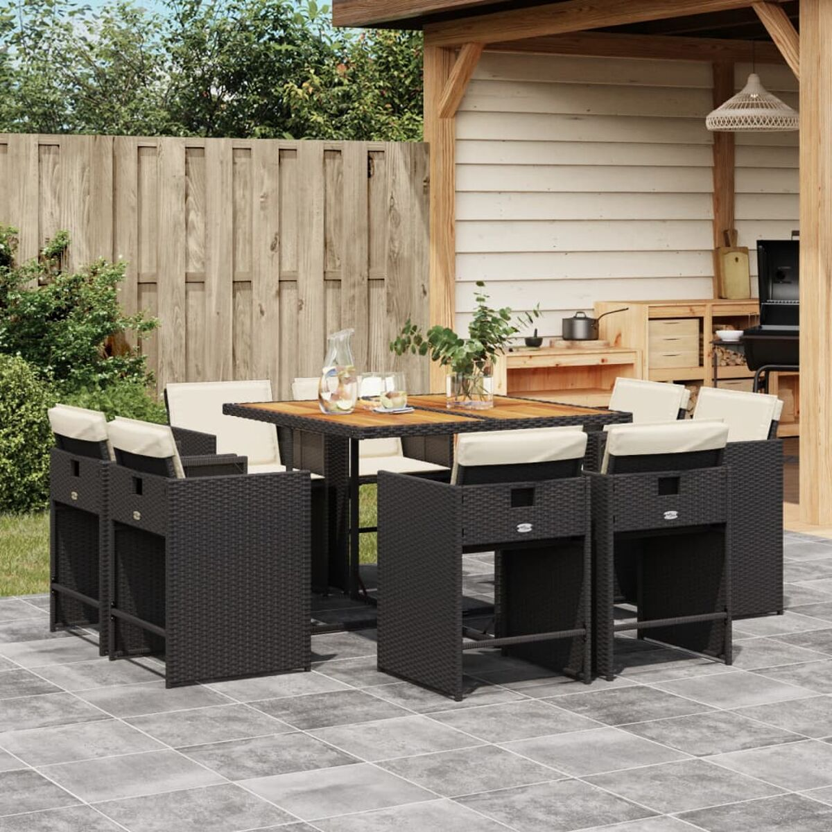Schwarzes Outdoor-Bar-Set aus Korbgeflecht mit weißen Kissen und einem Holztisch. Backstein-Terrasse.