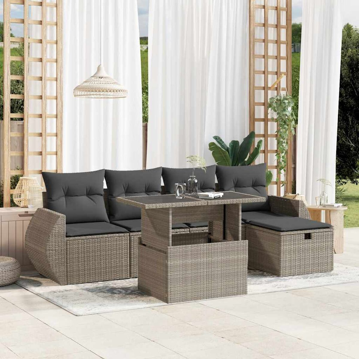 Terrassen-Set mit grauem Korbsessel, Couchtisch und Kissen. Weiße Vorhänge dahinter.