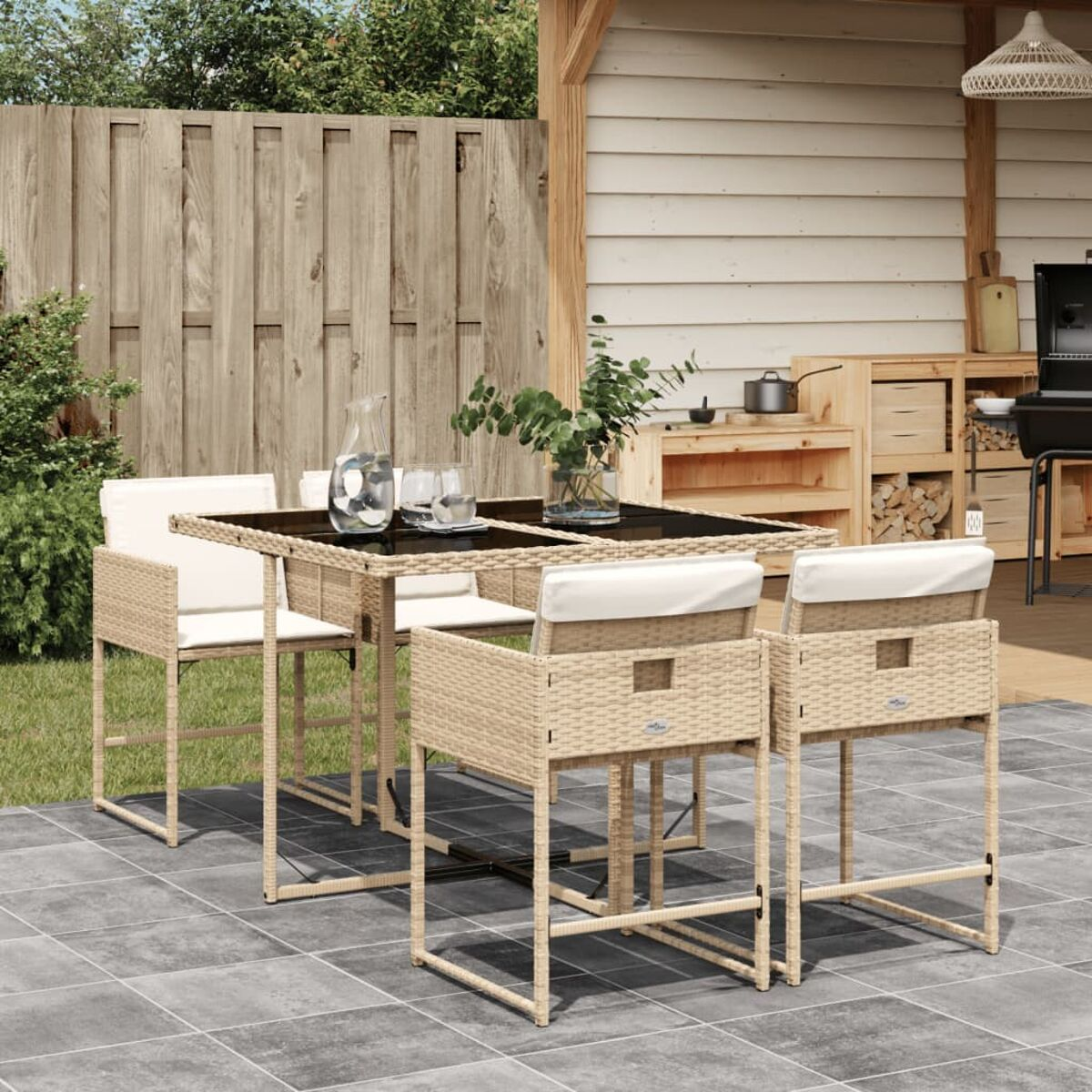 Set da pranzo all'aperto con tavolo quadrato e quattro sgabelli da bar. Sedie beige intrecciate con cuscini bianchi.