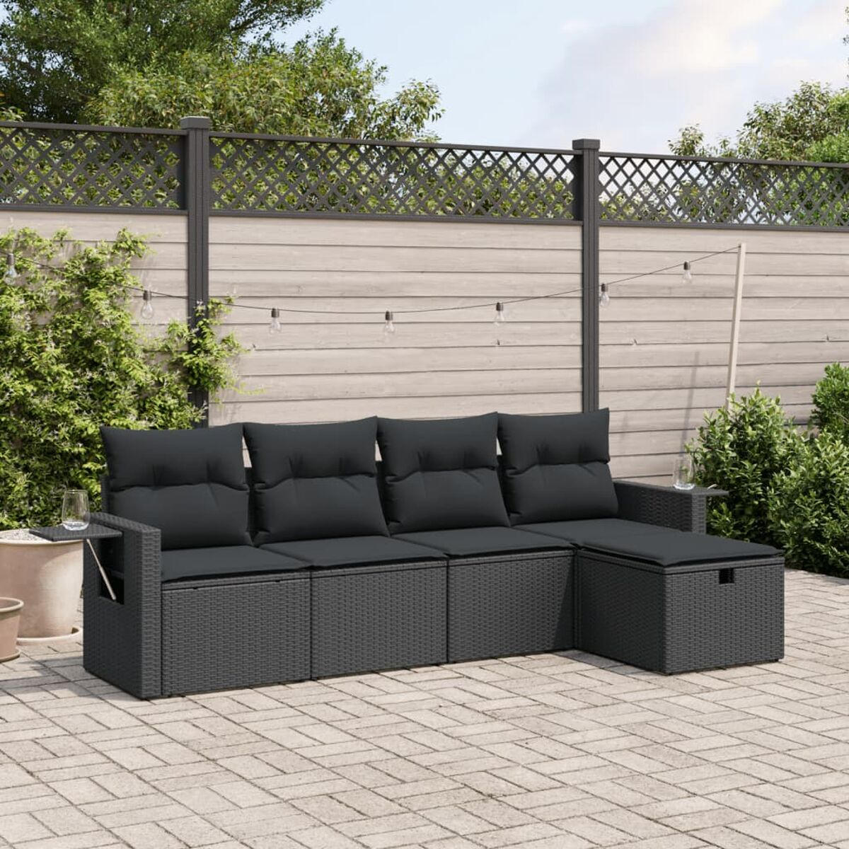 Dunkelgraues Ecksofa aus Korbgeflecht mit schwarzen Kissen auf einer Terrasse.