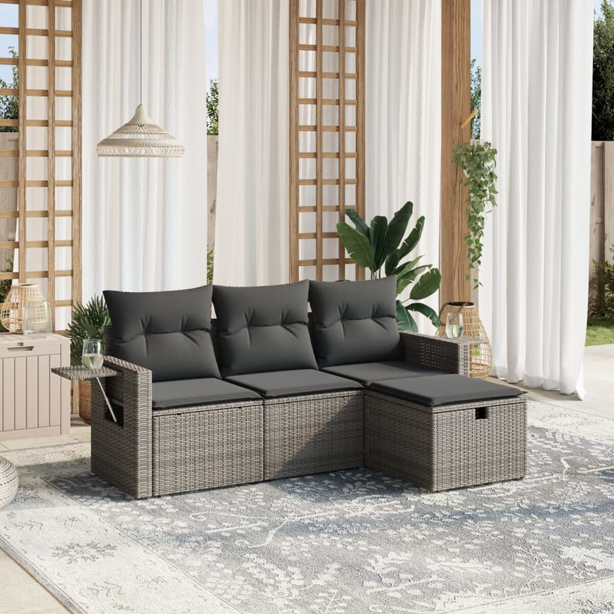 Graues Korbsessel-Sofa mit Kissen auf einem gemusterten Teppich. Weiße Vorhänge und Pflanzen schaffen eine entspannte Umgebung im Freien.
