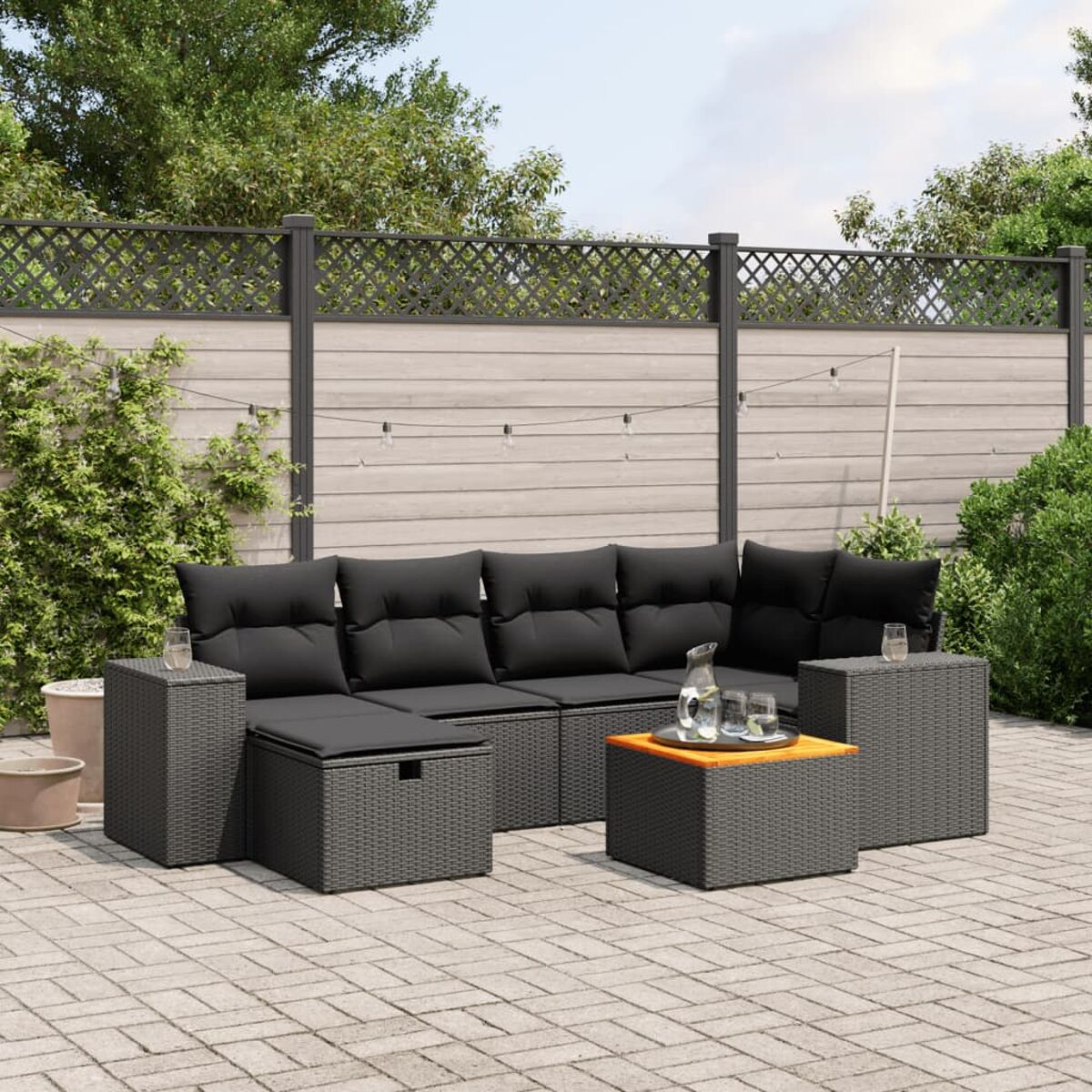 Dunkelgraues Rattan-Outdoor-Ecksofa mit schwarzen Kissen, Tisch, Gläsern und Wasserkrug auf der Terrasse.