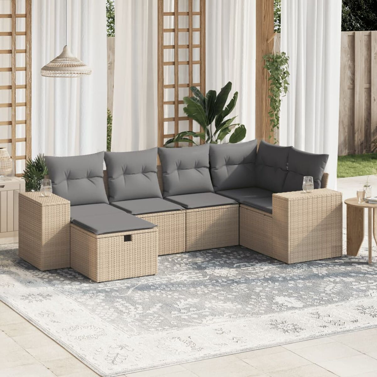 Ein beiges Outdoor-Sitzset aus Korbgeflecht mit grauen Kissen. Helle Teppich und Pflanzen im Hintergrund.