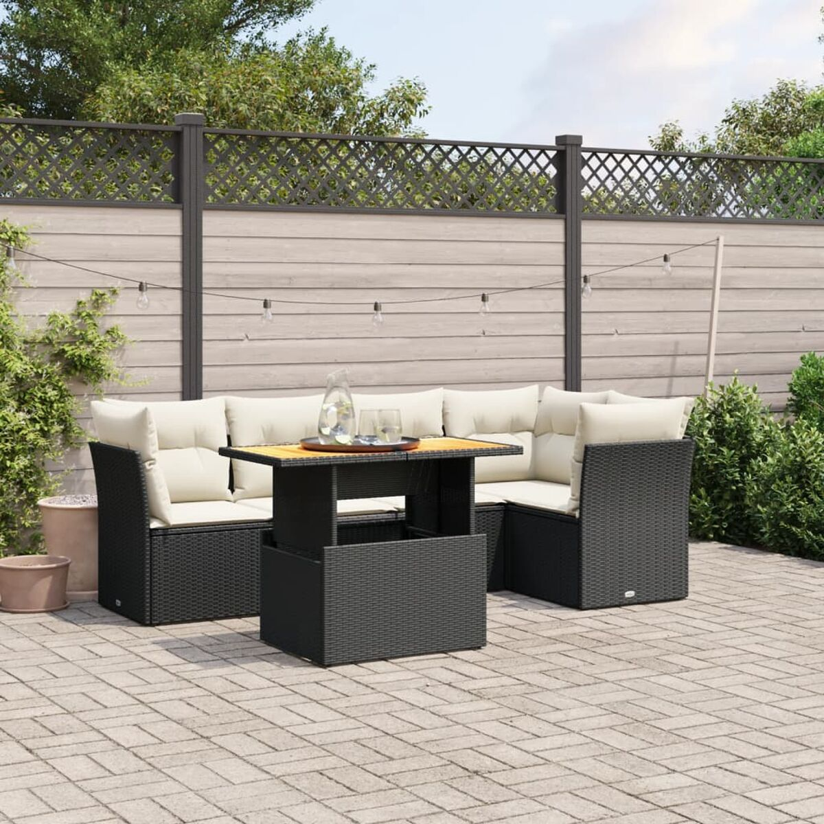 Outdoor schwarzes Korbgeflecht-Ecksofa-Set mit Tisch und Gartenzaun im Hintergrund.