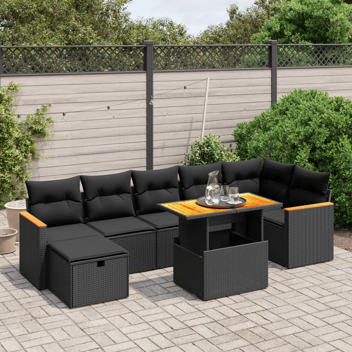 Schwarzes Outdoor-Ecksofa mit Tisch. Grüne Pflanzen umgeben es. Pflasterhintergrund.
