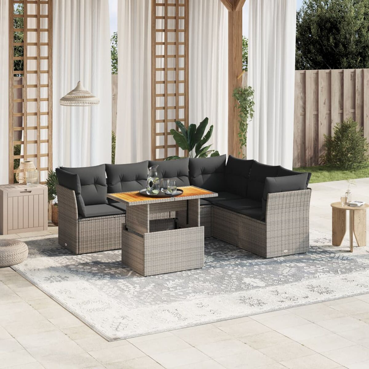 Scena di patio all'aperto con mobili intrecciati grigio chiaro, un tappeto e una tenda bianca.