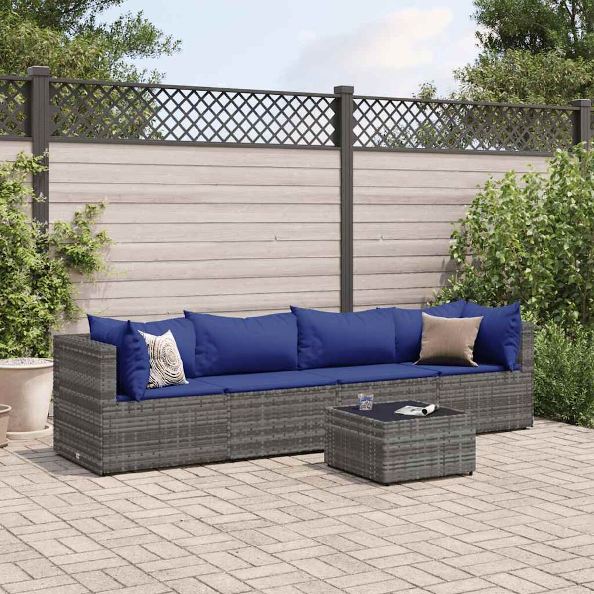 Graues Ecksofa für draußen mit blauen Kissen und einem schwarzen Tisch. Hintergrund: Zaun, Grün.