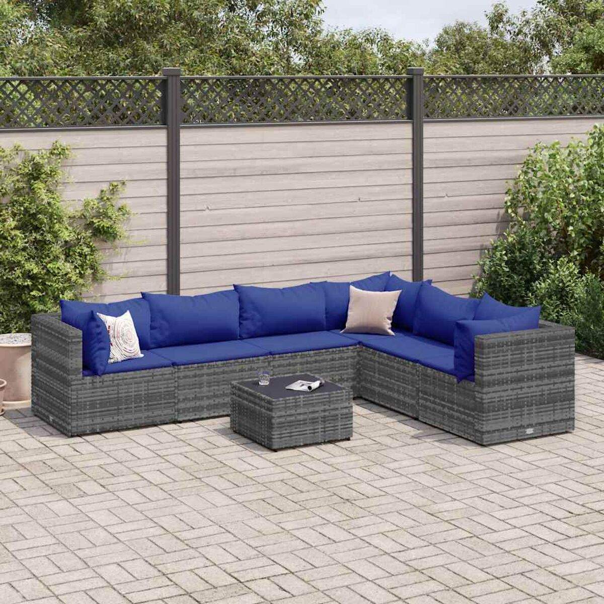 Set patio esterno con divano componibile, tavolino e cuscini blu. Sfondo verde.