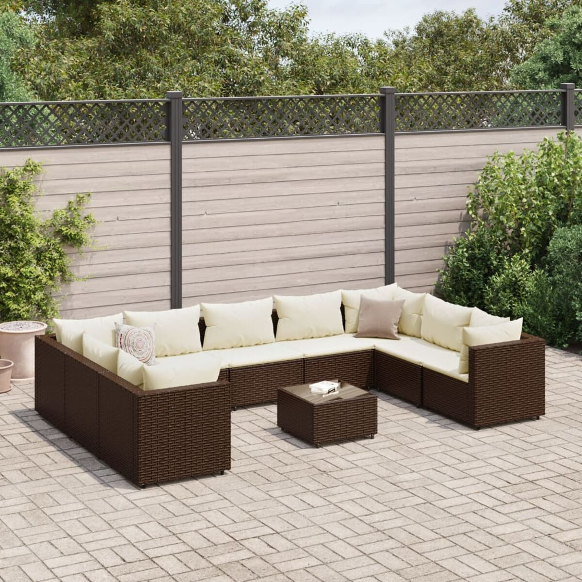Divano angolare in vimini marrone scuro con tavolo e cuscini color crema. Su un patio in mattoni.
