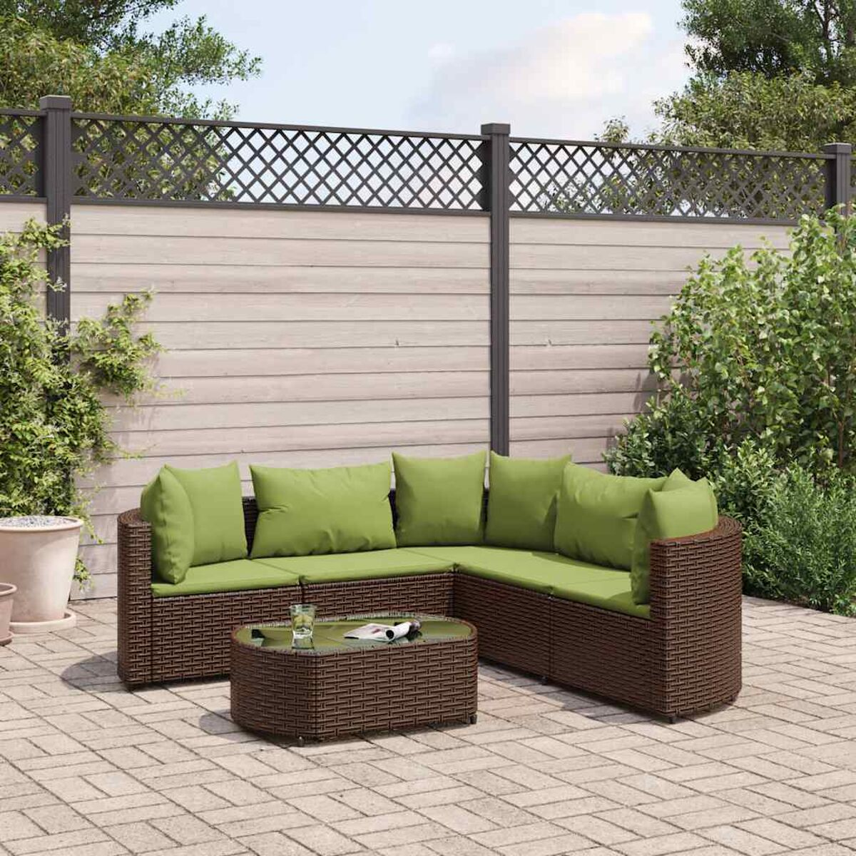 Braunes Korbmöbel mit grünen Kissen und einem Tisch auf einer Terrasse mit Zaun.