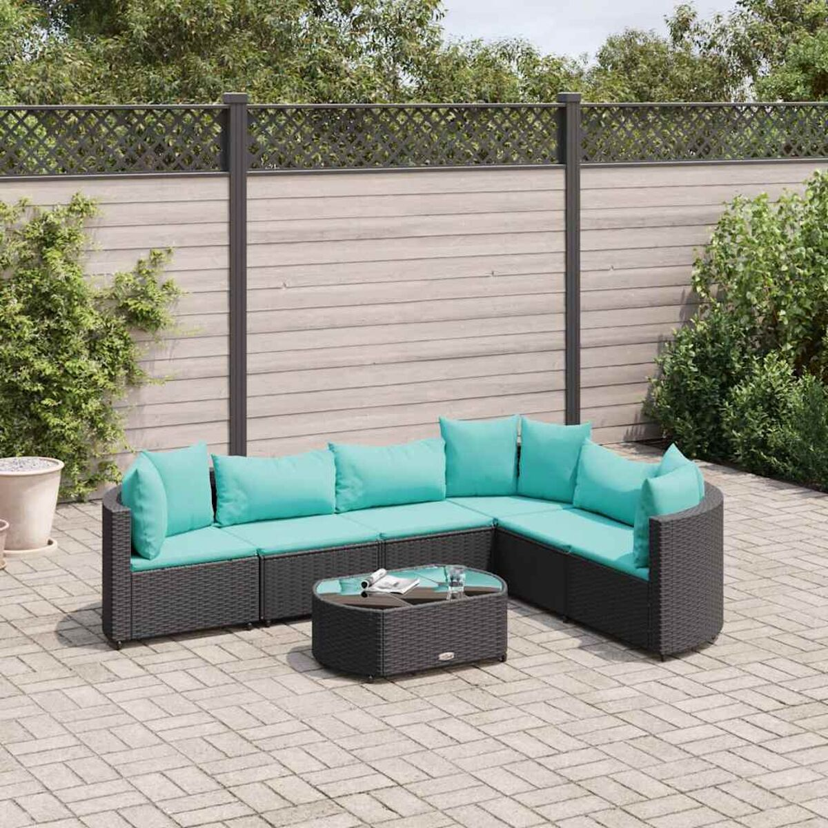 Divano componibile in vimini nero con cuscini turchesi. Tavolo rotondo in vetro. Il set è su un patio.