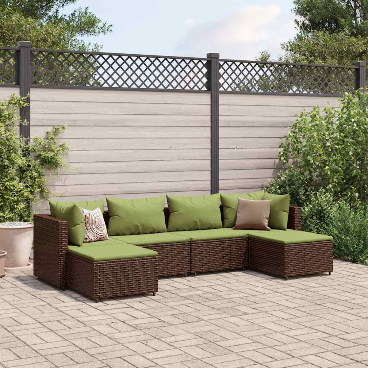 Braunes Rattansofa-Set mit grünen Kissen in einem Garten. Grüne Pflanzen sichtbar.