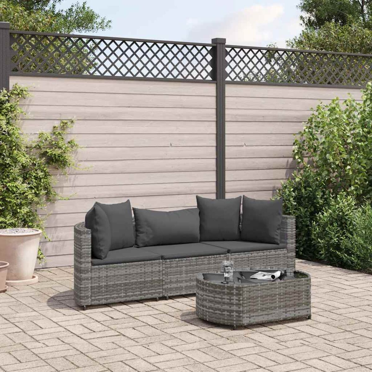 Set divano in vimini grigio con cuscini grigi e un tavolino. Una recinzione e un patio sono sullo sfondo.