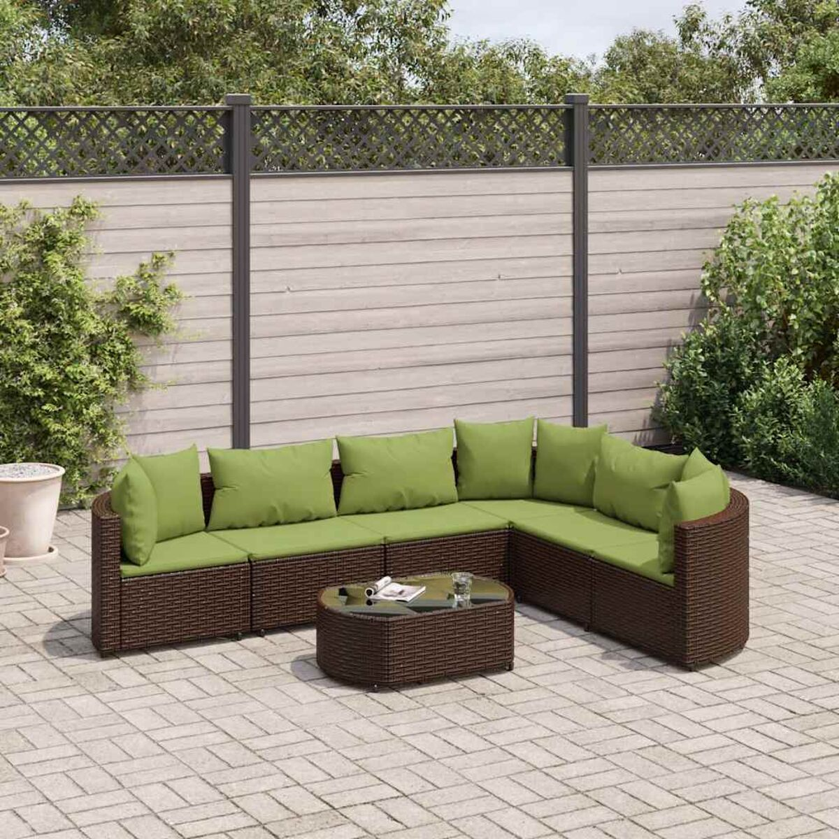 Braunes Outdoor-Ecksofa aus Korbgeflecht mit grünen Kissen und einem passenden Couchtisch auf einer Steinterrasse.