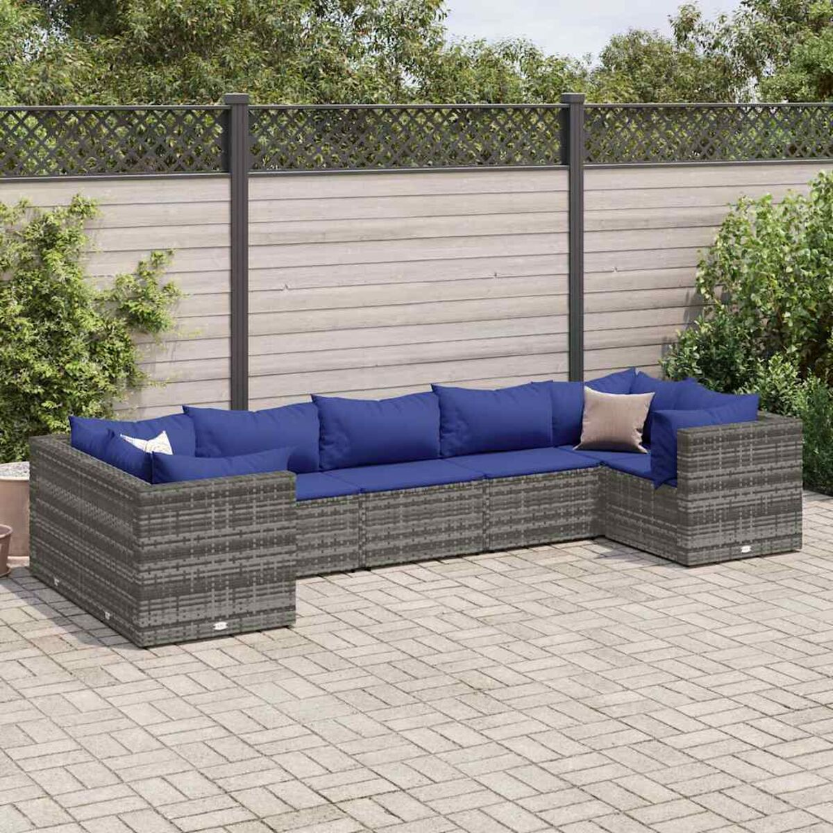 Asientos exteriores en forma de U de mimbre gris sobre un patio de ladrillos. Cojines azules y una valla.