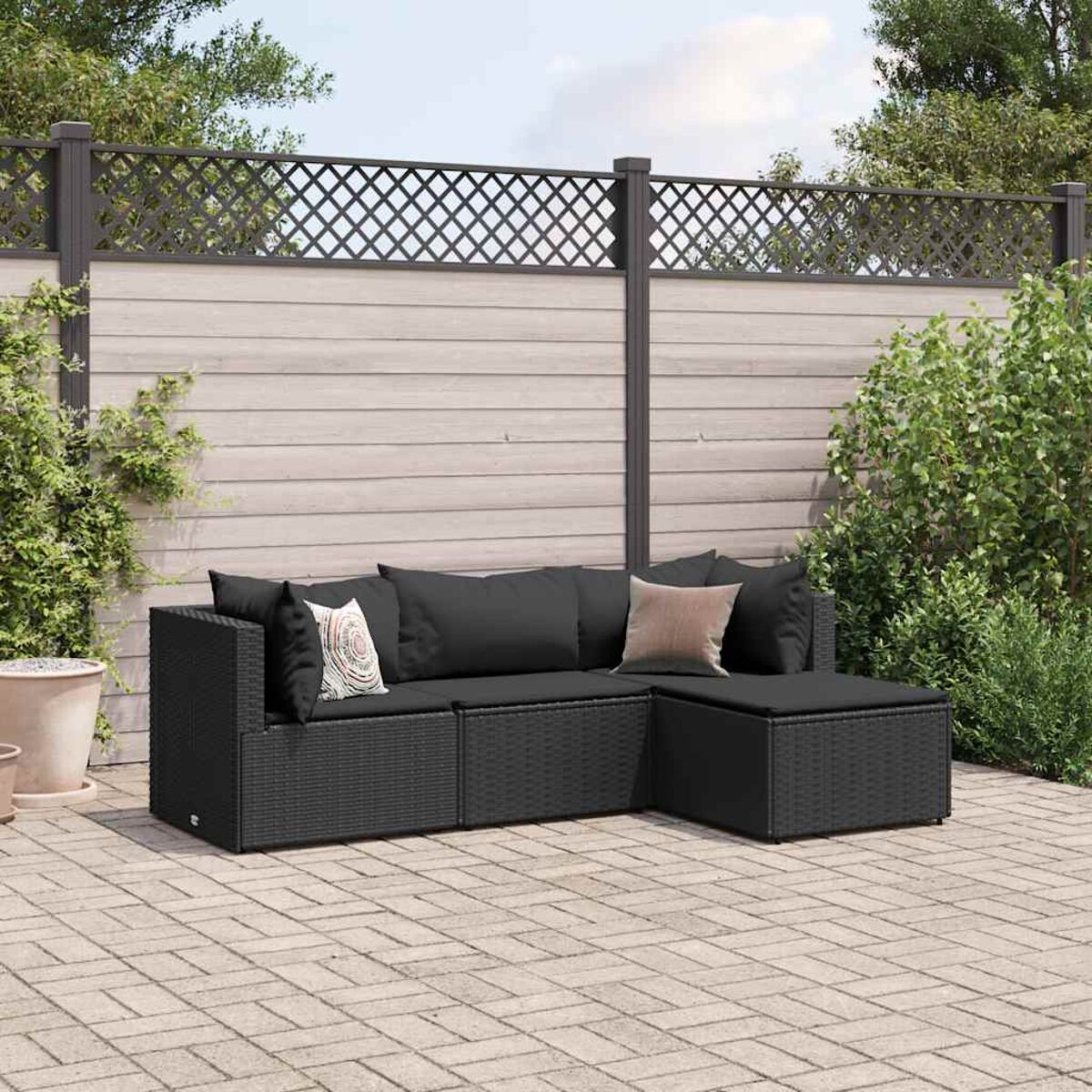 Divano componibile da esterno in vimini nero con cuscini. Patio in pietra e sfondo di recinzione in legno.