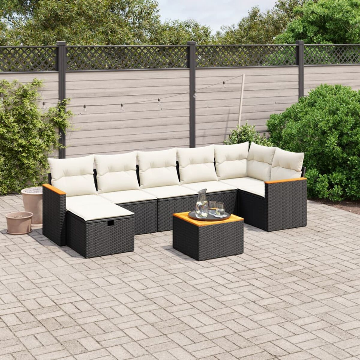 Outdoor-Sitzgruppe mit schwarzen Kissen und Tisch. Grün und Zaun im Hintergrund.
