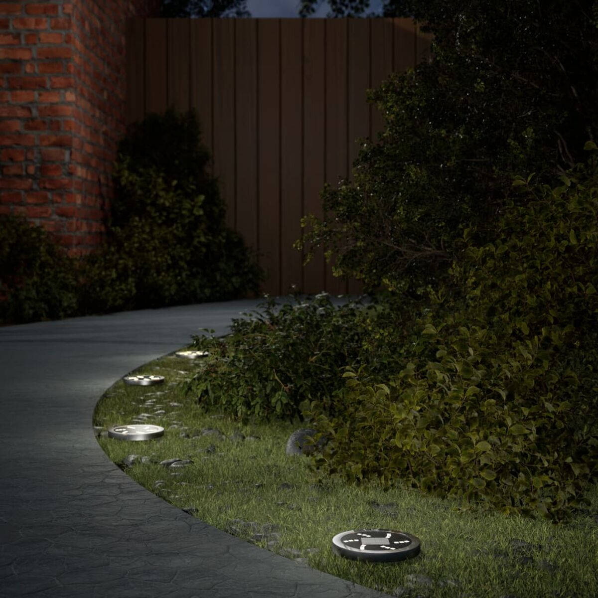 Gartenweg bei Nacht, beleuchtet mit kleinen, runden Bodenlichtern. Bäume und ein Zaun.