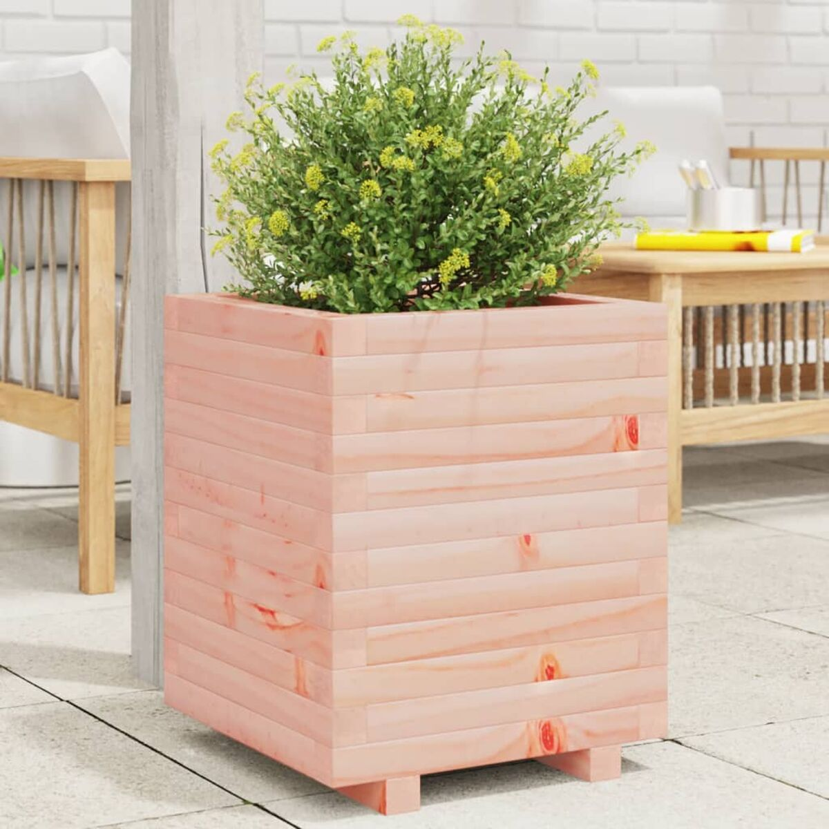 Ein Holzpflanzgefäß mit einer grünen Pflanze. Es steht auf einer Terrasse mit Tisch und Stuhl.