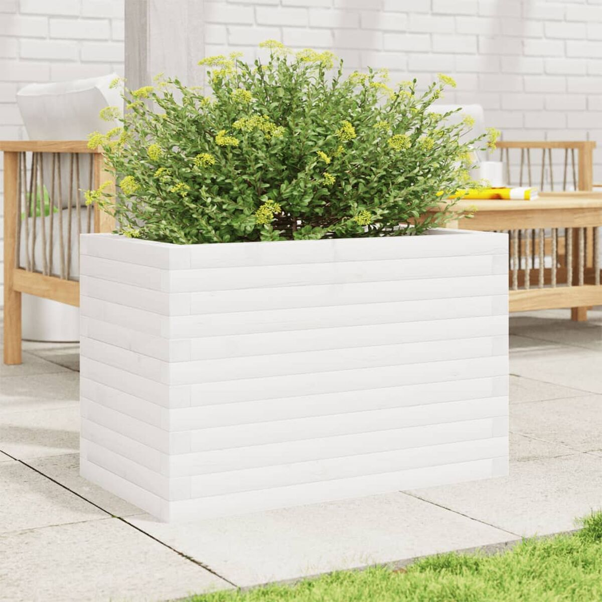 Weißer Holz-Pflanzkasten mit grünen Blättern und gelben Blüten, auf Terrasse. Ziegelmauer im Hintergrund.