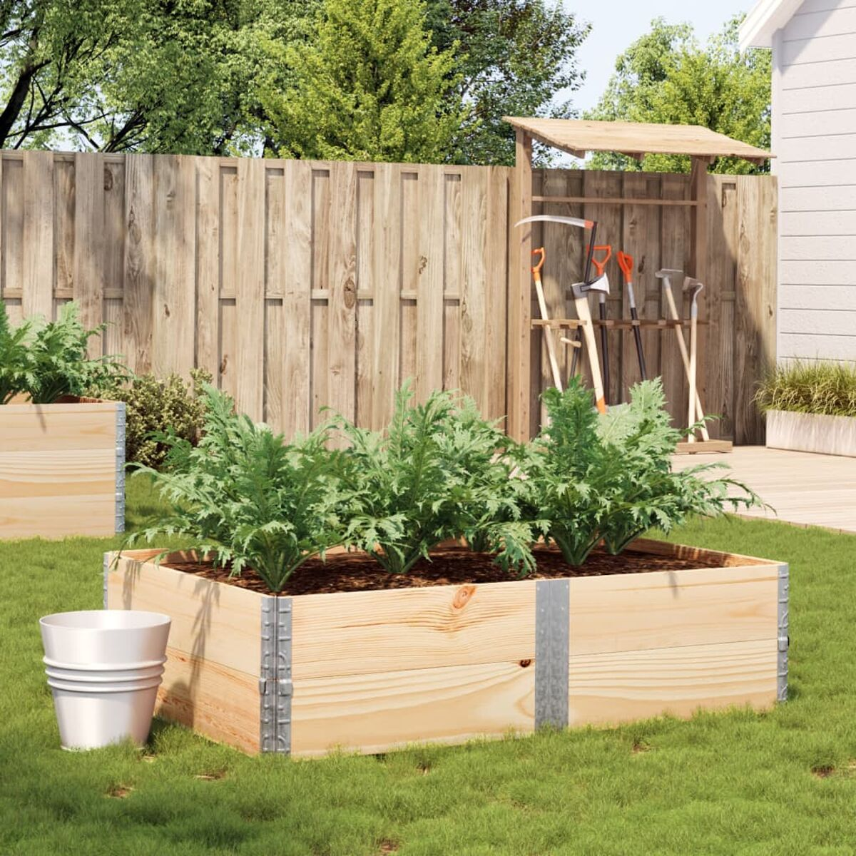 Erhöhtes Gartenbeet mit Pflanzen, Werkzeugen und Eimer.