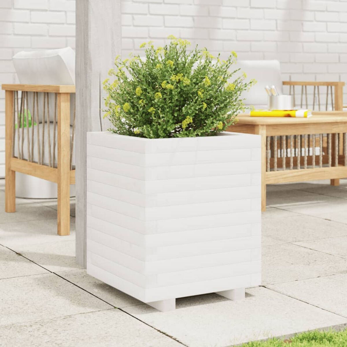 Weißer quadratischer Pflanzkübel mit grüner Pflanze. Andere Gartenmöbel sind im Hintergrund.