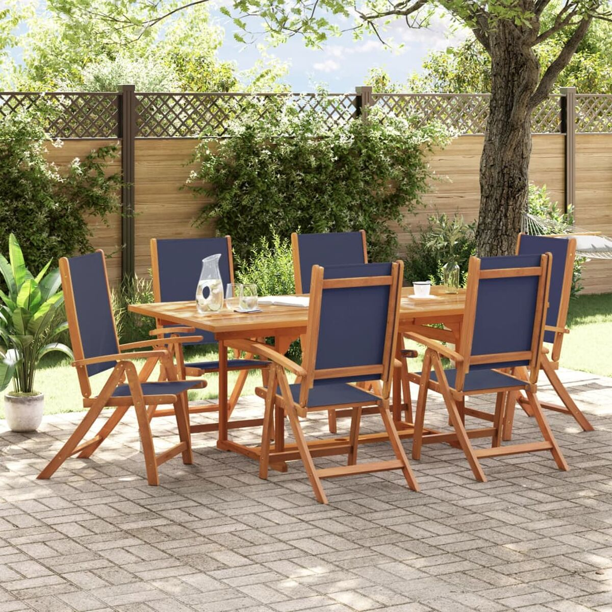 Tavolo in legno con sei sedie con sedili blu in un giardino, vicino a una recinzione e alberi.