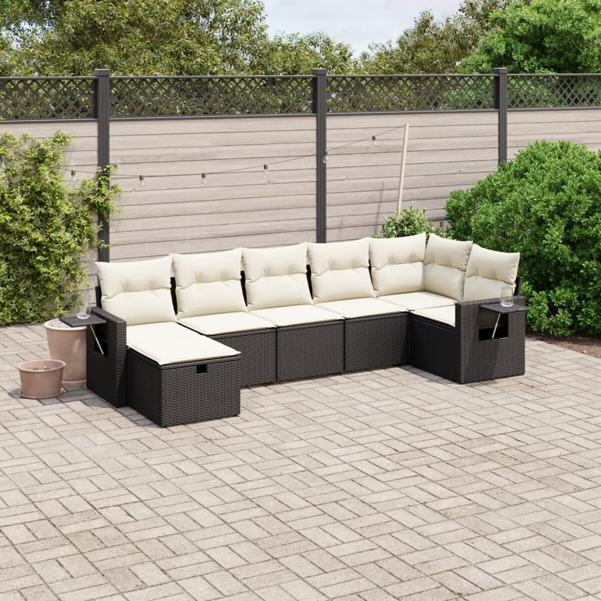 Schwarzes Rattan-Outdoor-Ecksofa mit cremefarbenen Kissen auf einer gepflasterten Terrasse.