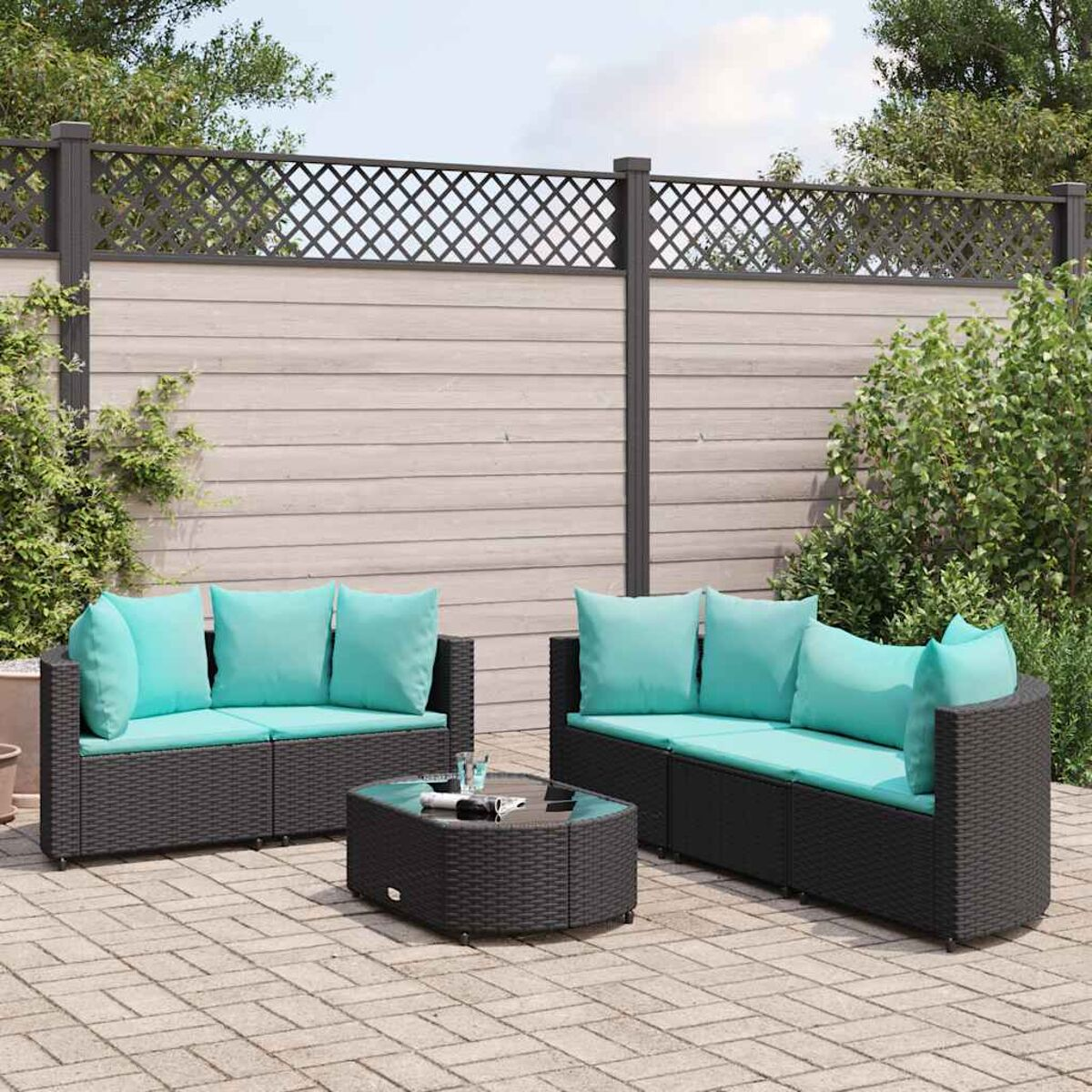 Set di mobili da patio esterno con una recinzione bianca e vegetazione sullo sfondo. I mobili sono neri.