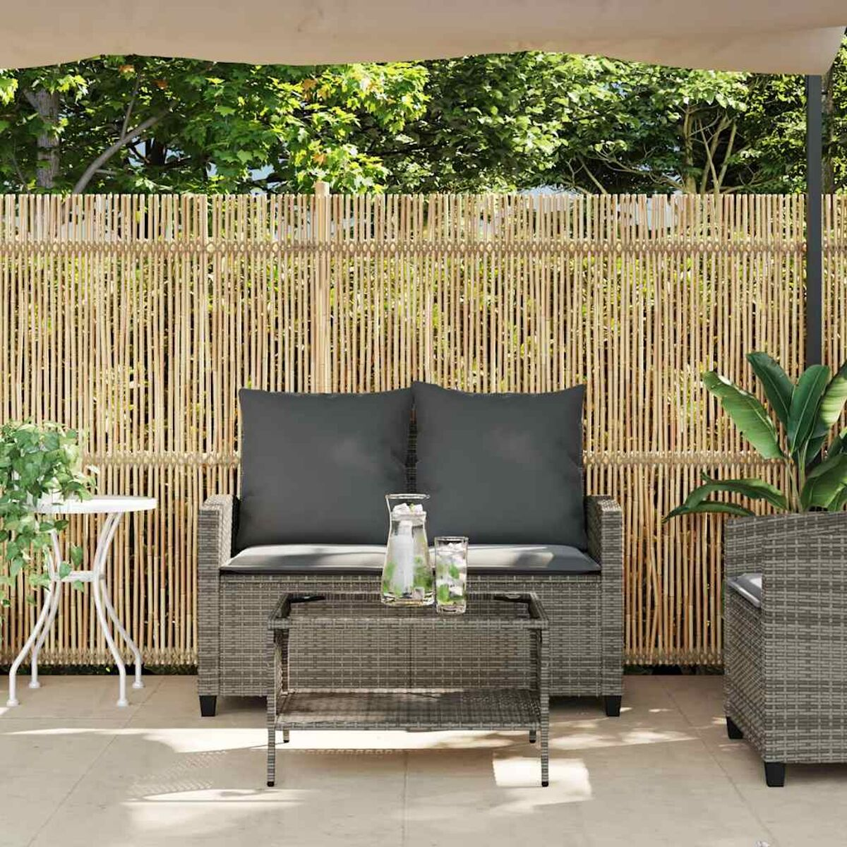 Patio con divano in rattan, cuscini e un tavolino. Una recinzione in bambù sullo sfondo.