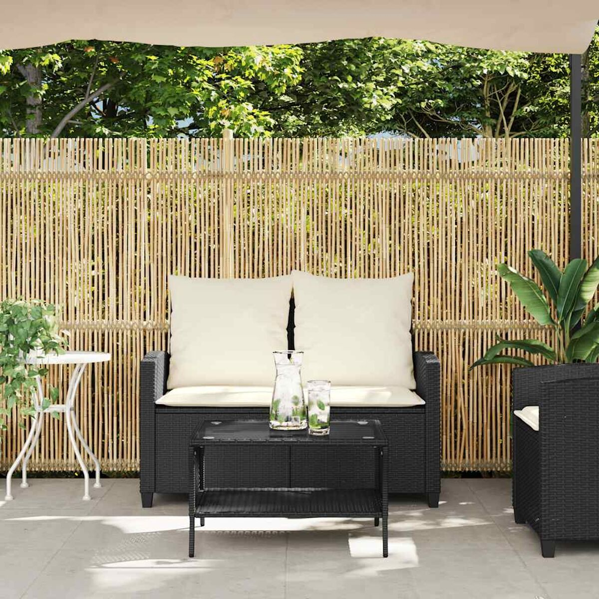 Conjunto exterior con sofá, mesa auxiliar y de centro, todo negro, con valla de bambú.