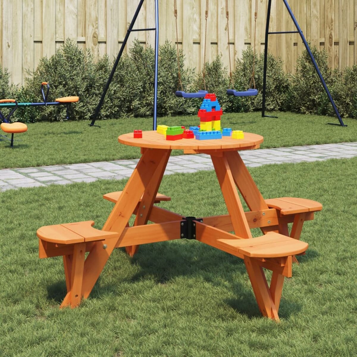 Holz-Picknicktisch mit angebrachten Bänken. Farbige Blöcke auf dem Tisch. Grünes Gras und Schaukeln im Hintergrund.