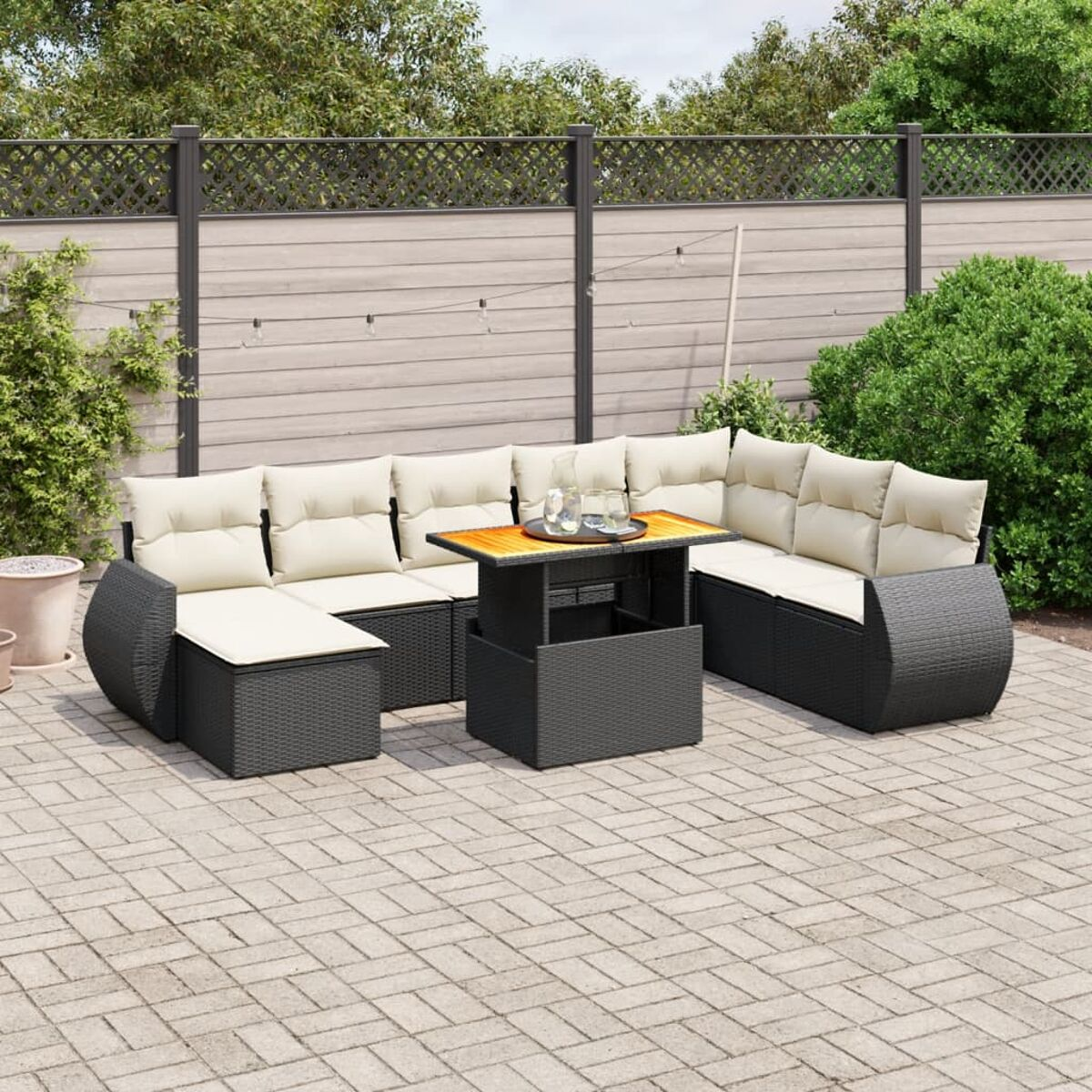 Outdoor-Möbelset aus schwarzem Korbgeflecht mit beigefarbenen Kissen, einem Tisch und einer gemusterten Ziegelterrasse.