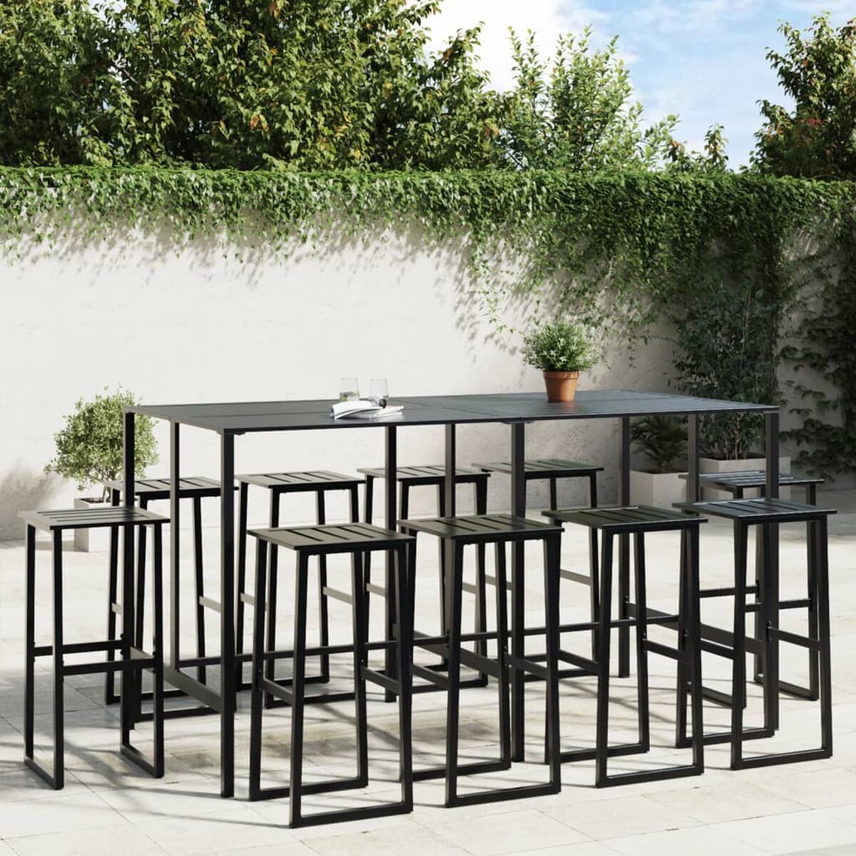 Tavolo da bar all'aperto con sgabelli, struttura in metallo nero, su un patio con vegetazione.