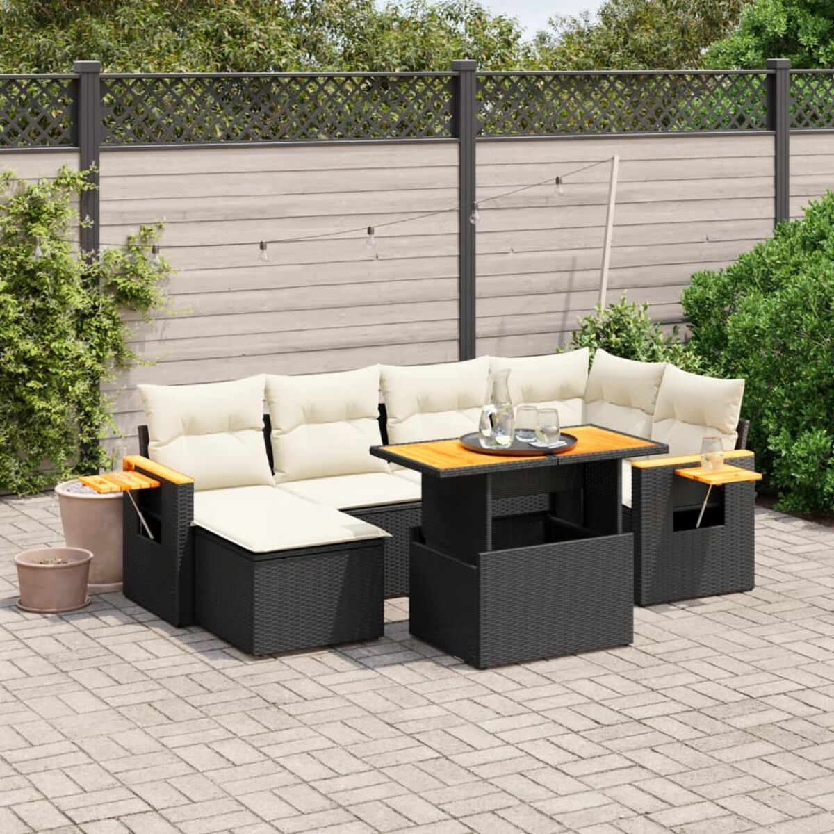 Schwarzes Gartenmöbel-Set mit Tisch auf einer Backstein-Terrasse mit Pflanzen im Hintergrund.