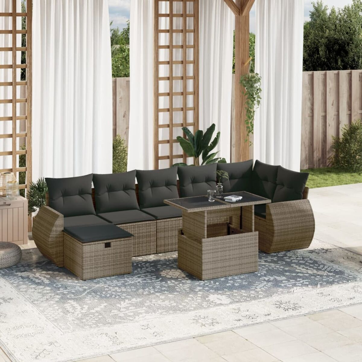 Außenbereich mit einem Rattan-Sofa, einem Couchtisch und weißen Vorhängen. Der Tisch ist hochgestellt.