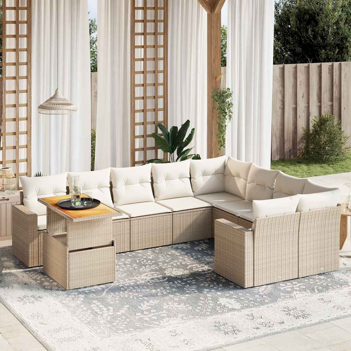 Set di mobili da patio all'aperto. Divani e tavolo beige con tappeto grigio. Tende bianche e recinzione in legno sullo sfondo.