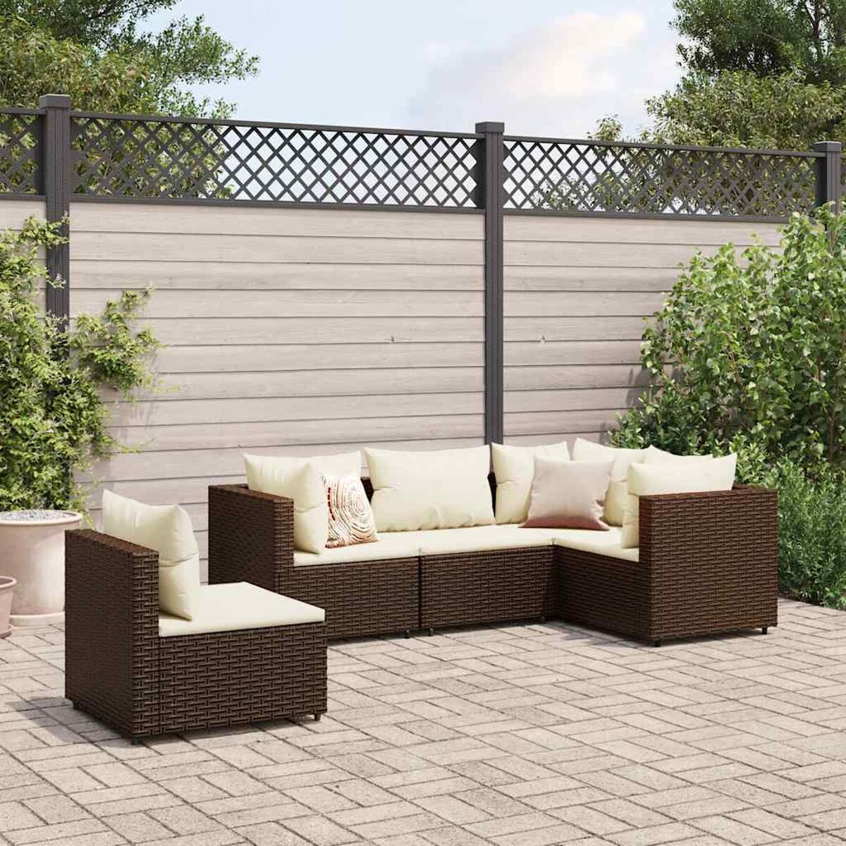 Set di mobili da esterno in rattan marrone con cuscini beige, contro una recinzione e vegetazione.