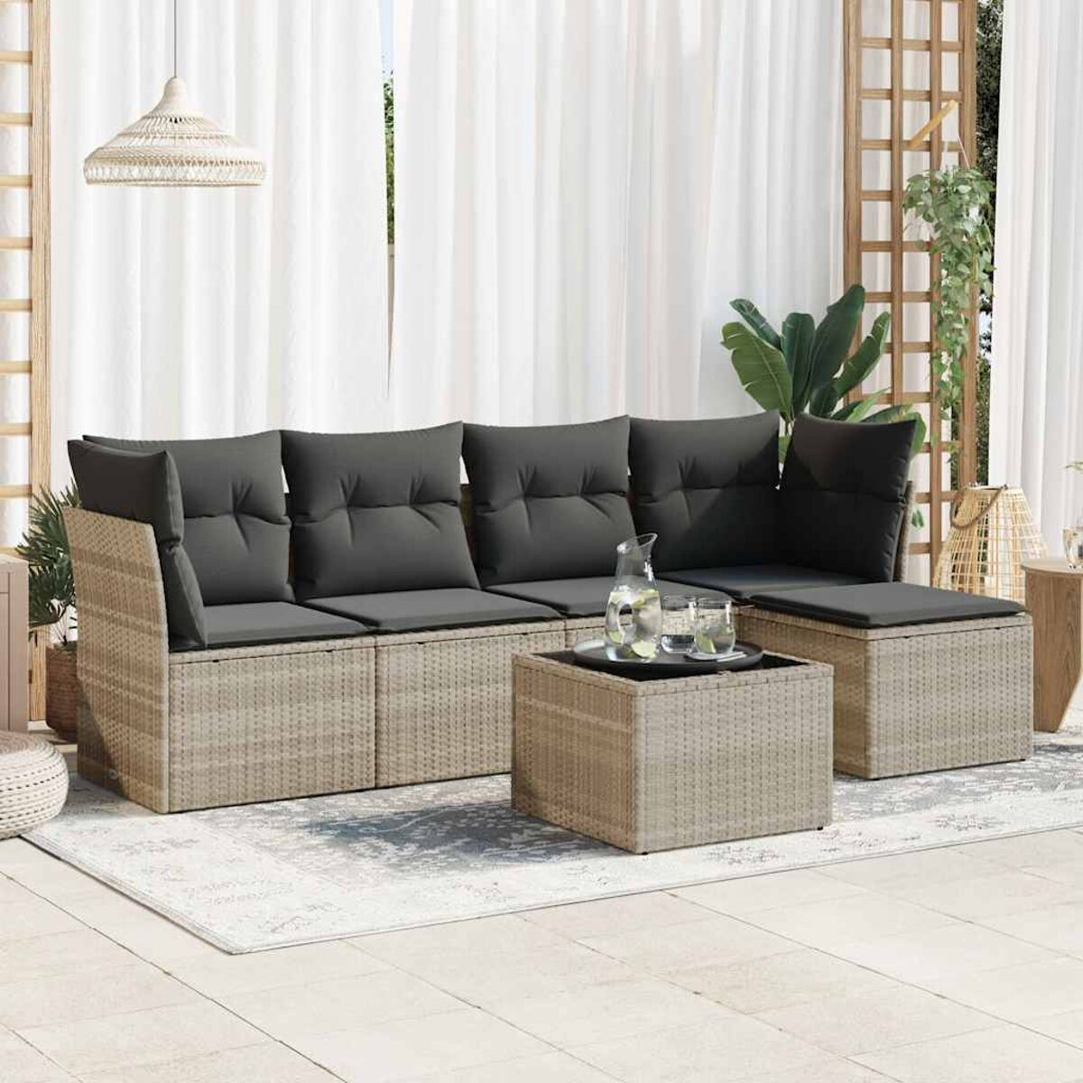 Geflochtenes Sofaset mit dunklen Kissen und einem quadratischen Tisch. Weiße Vorhänge im Hintergrund.
