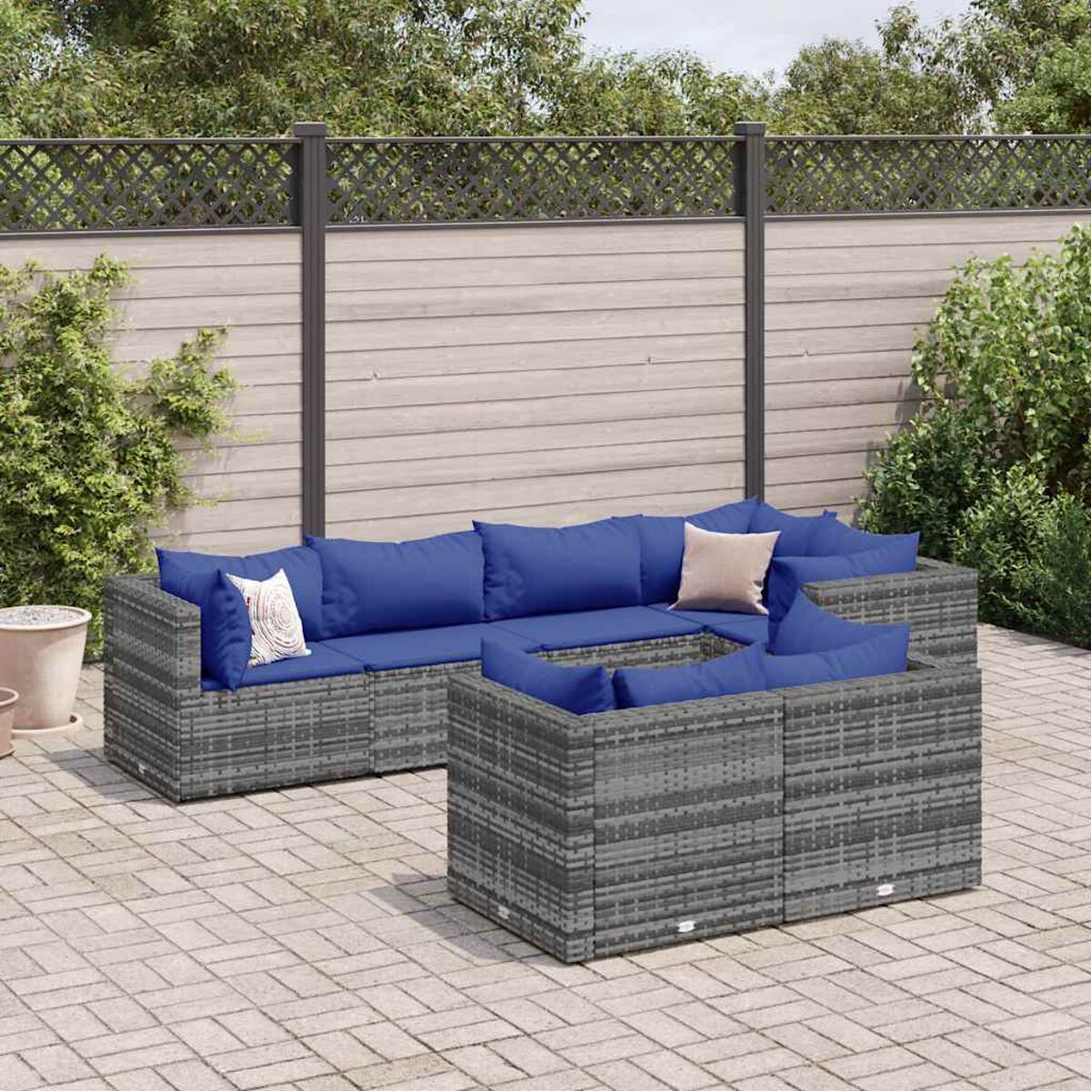 Eine Outdoor-Terrassengarnitur mit einem grauen Korbsessel mit blauen Kissen und einem neutralen Kissen.